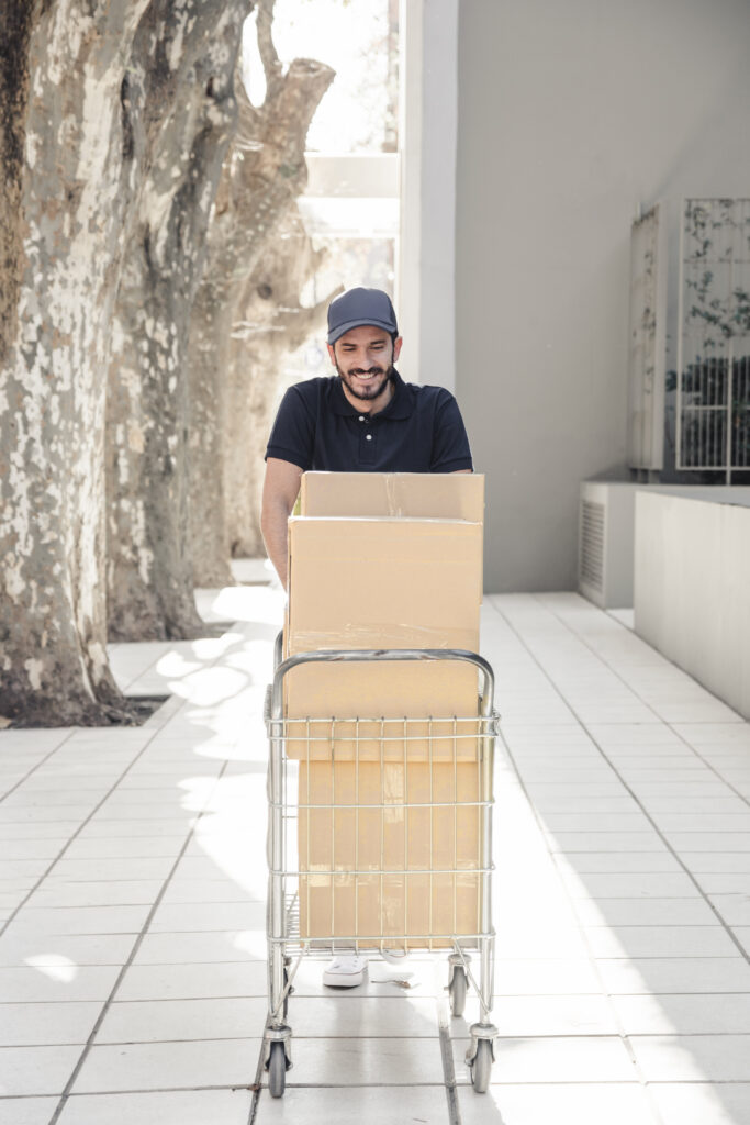smiling delivery man walking pavement with trolley full cardboard boxes smiling delivery man walking pavement with trolley full cardboard boxes